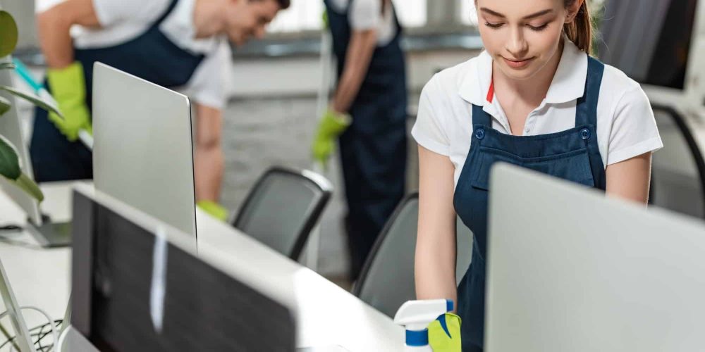 selective-focus-of-pretty-cleaner-wiping-desk-while-colleagues-cleaning-floor-in-office.jpg