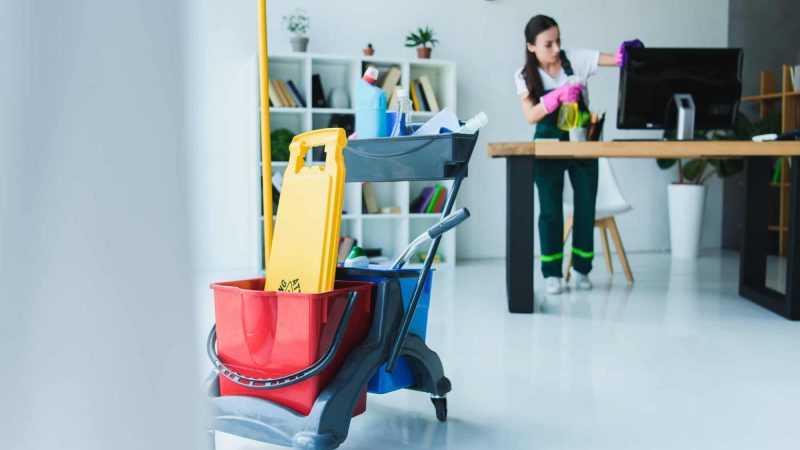 young-female-janitor-cleaning-office-with-various-cleaning-equipment.jpg